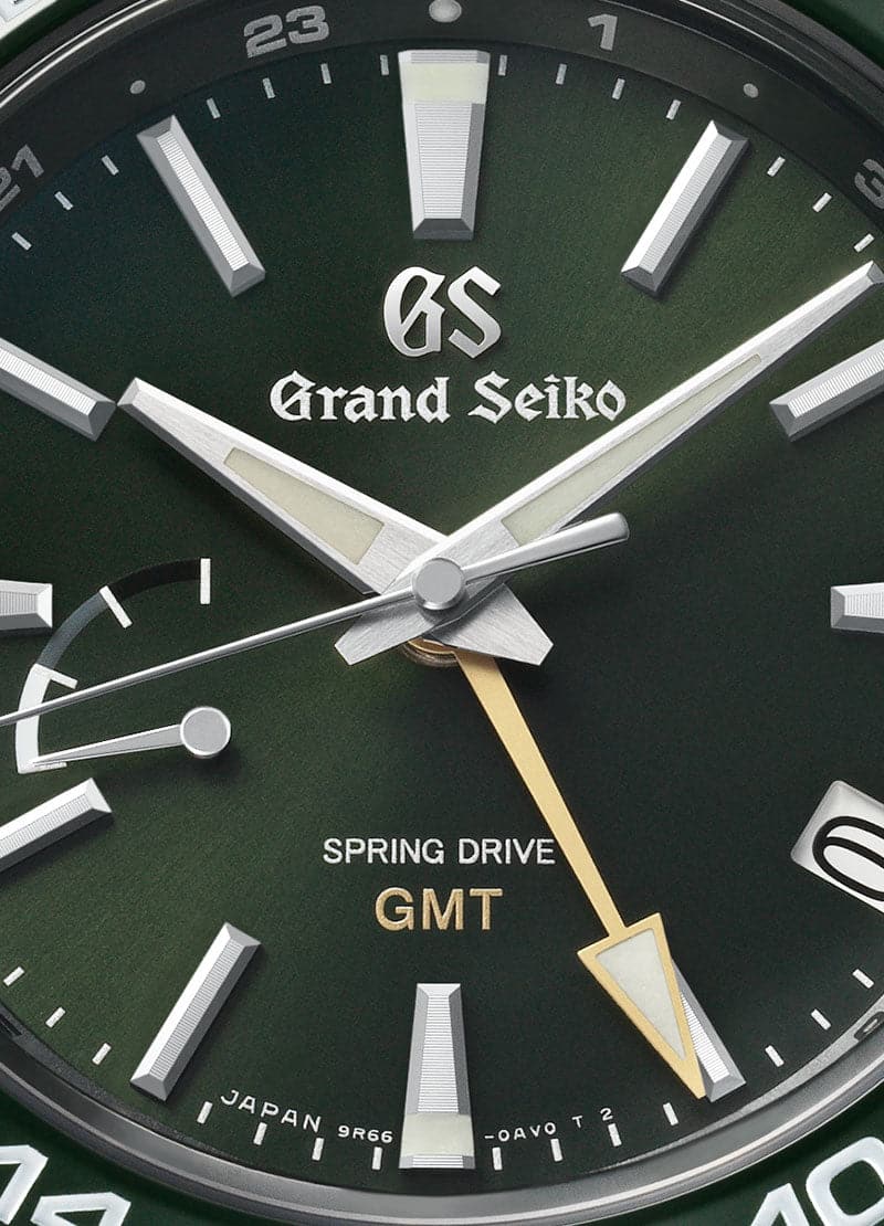 Detailed close-up perspective view of the Grand Seiko SBGE257 watch face, highlighting the glossy green ceramic 24-hour bezel, the sunray-finished dark green dial, the yellow-gold GMT hand, and the power reserve indicator scale.