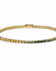 A gold tennis bracelet featuring a gradient of gemstones transitioning from yellow-green on one end to deep green on the other, displayed on a clean white background.