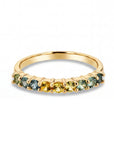 A gold ring featuring a row of small, round-cut gemstones in shades of yellow, light green, and blue, set against a clean white background.
