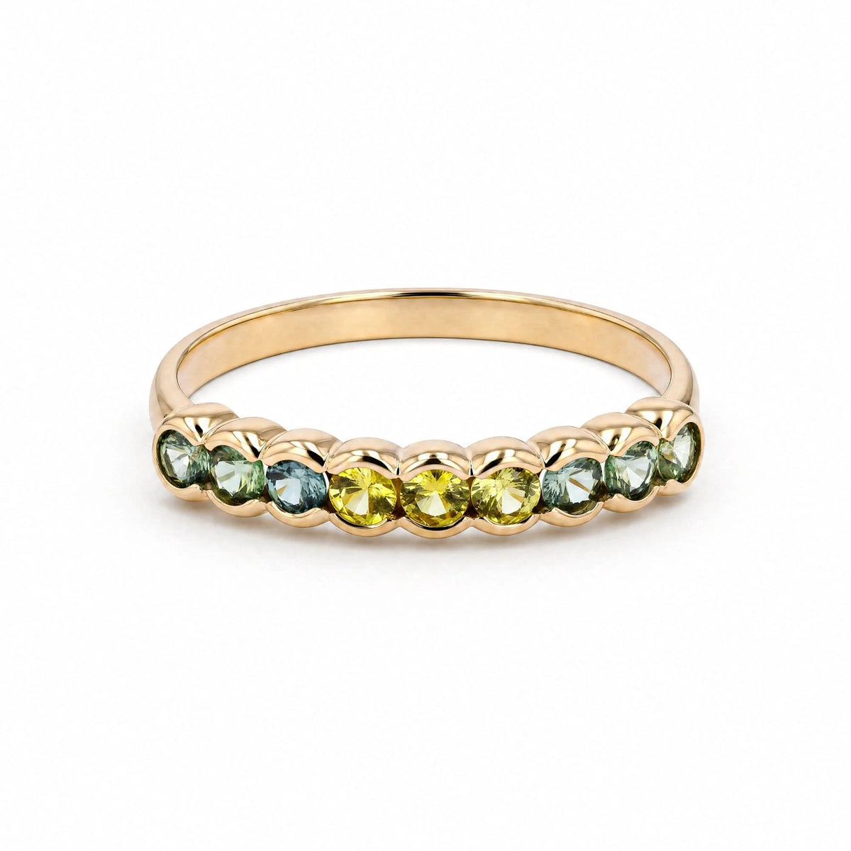 A gold ring featuring a row of faceted gemstones in shades of green, blue, and yellow, set against a clean white background.