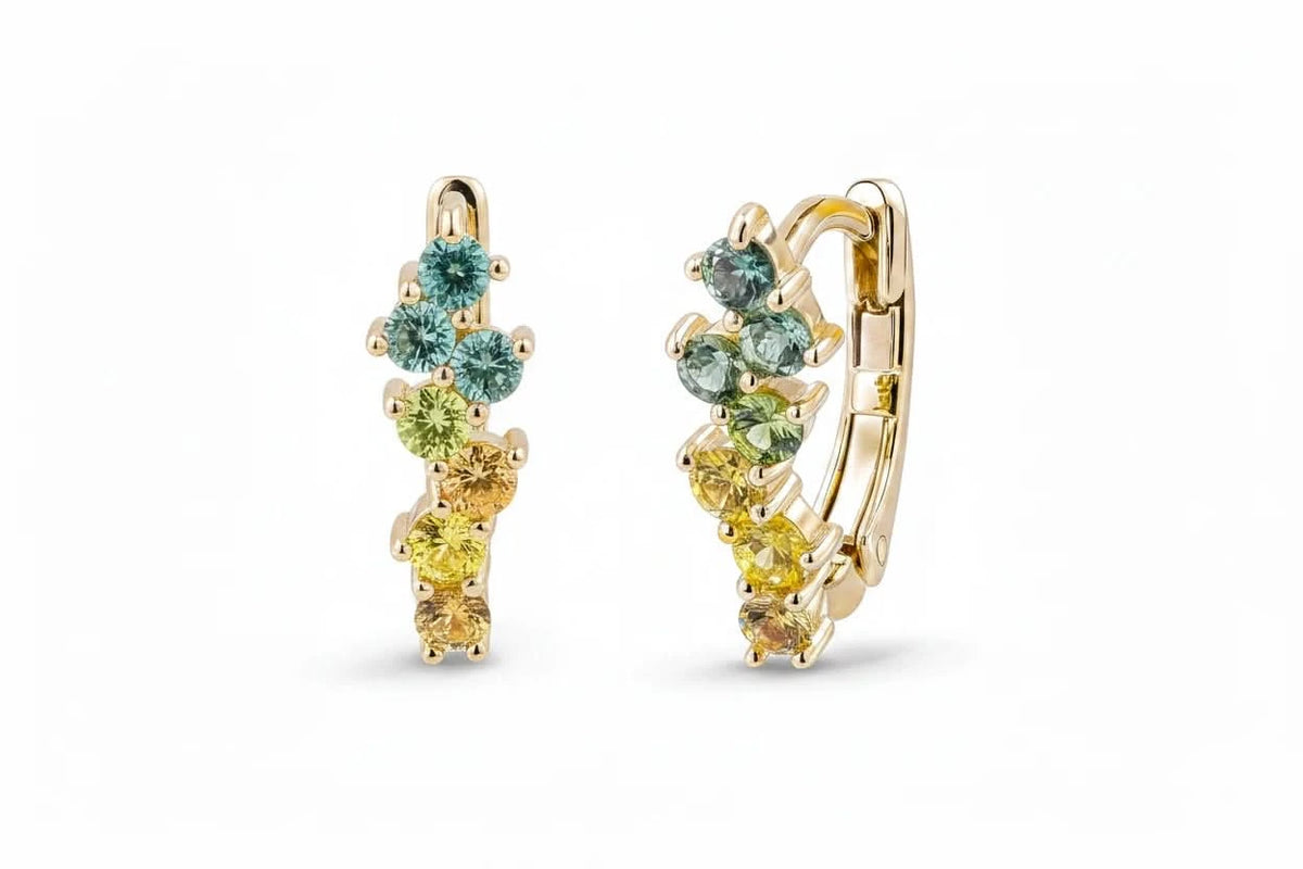 A gold huggie hoop earring featuring a row of small round-cut gemstones in green, yellow, and peach tones, set against a clean white background.
