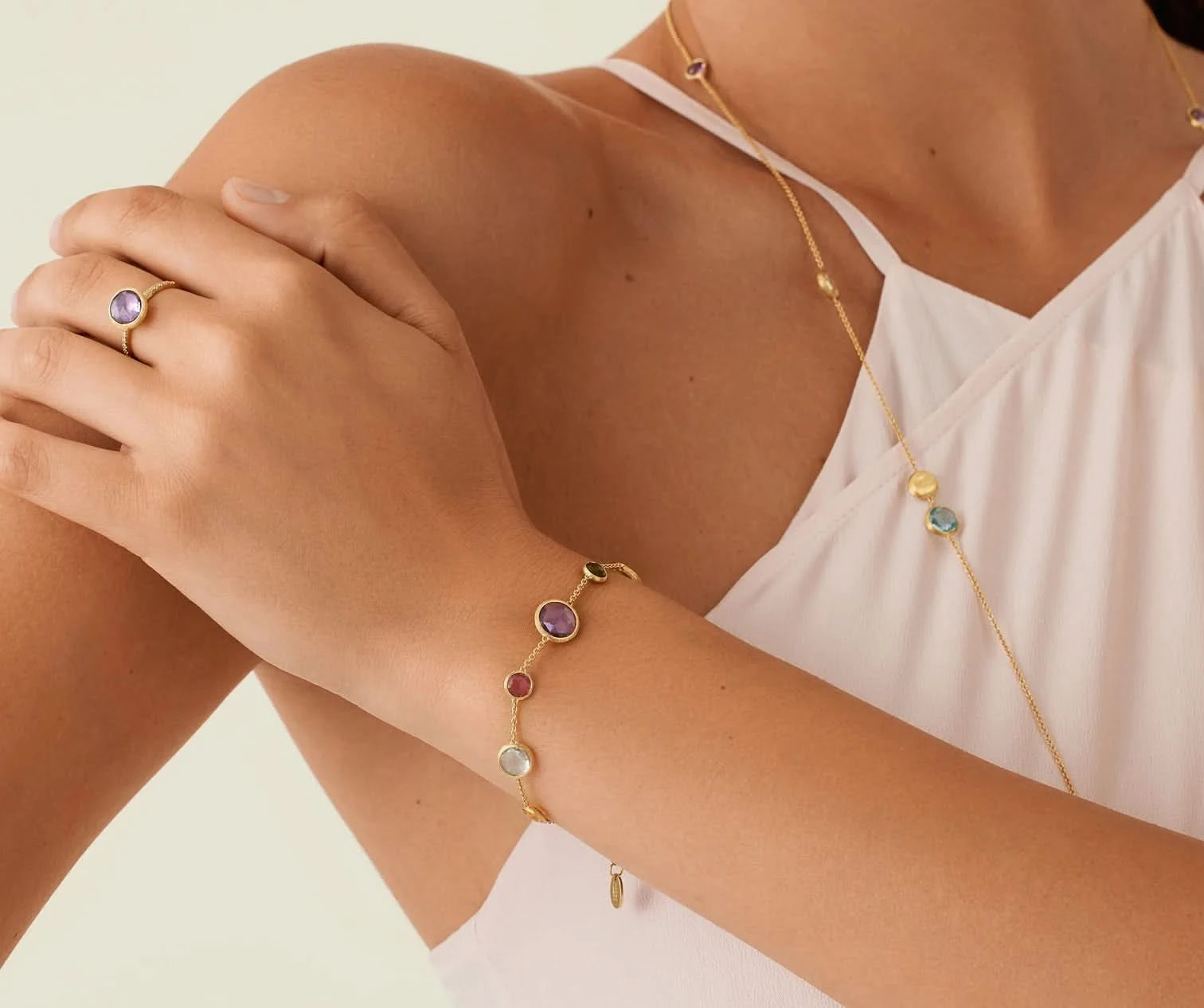 Close-up of a person wearing a gold bracelet with colorful gemstones on a light background