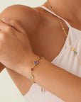 Close-up of a person wearing a gold bracelet with colorful gemstones on a light background