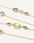 Three delicate gold chain necklaces with oval and round multicolored gemstones, arranged diagonally on a clean white background.