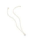 A delicate gold chain necklace with a small circular pendant featuring a halo of tiny clear stones, displayed on a solid off-white background.