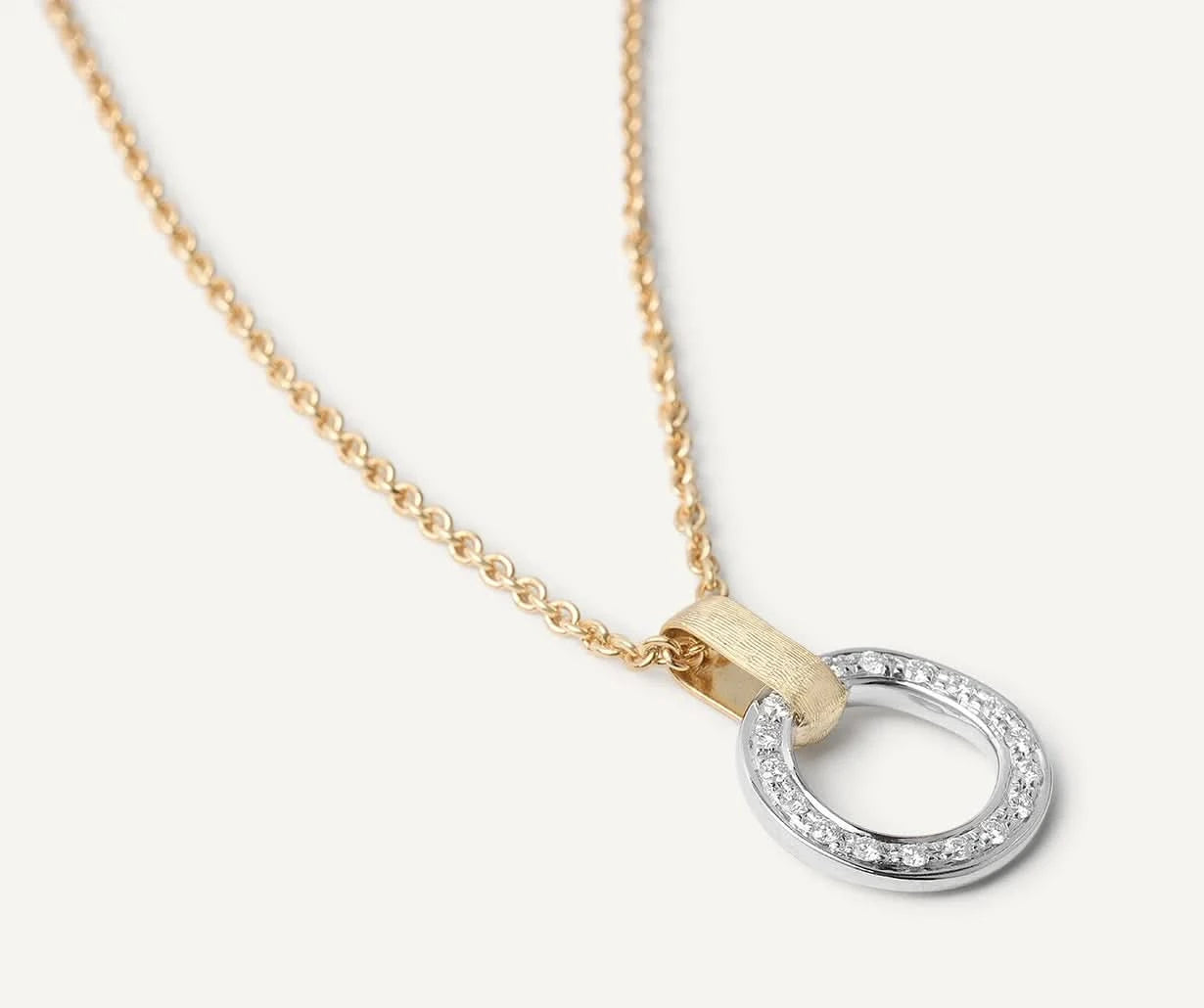 A delicate gold chain necklace featuring a modern open oval pendant with a textured gold top bar and a silver-toned bottom half encrusted with small clear stones, shown on a light cream background.