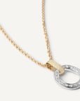A delicate gold chain necklace featuring a modern open oval pendant with a textured gold top bar and a silver-toned bottom half encrusted with small clear stones, shown on a light cream background.