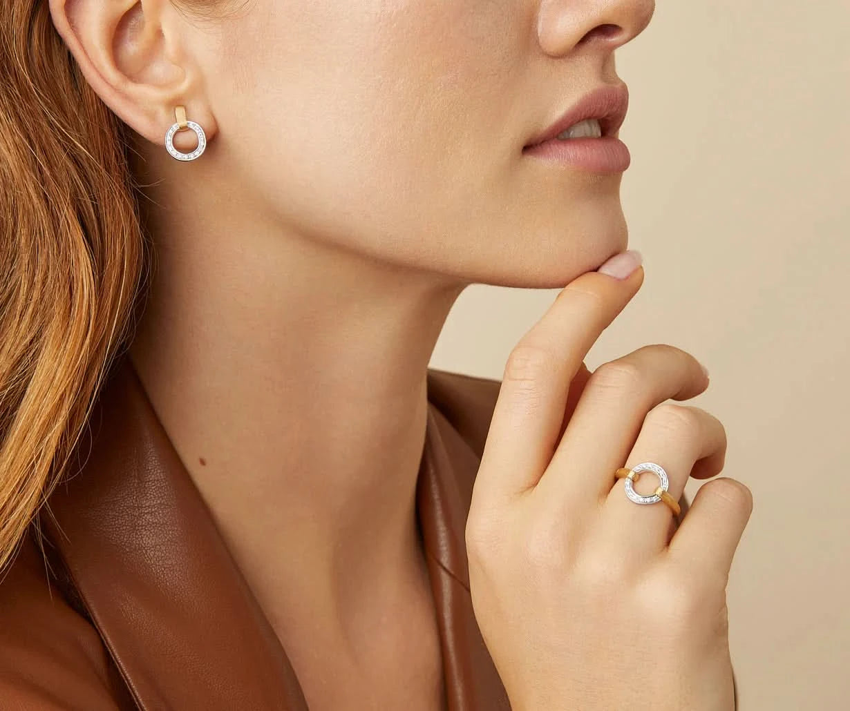 Close-up of a woman wearing silver tone and gold hoop earrings and a ring on a beige background