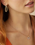 Close-up of a woman wearing gold hoop earrings and a gold necklace with a small pendant.