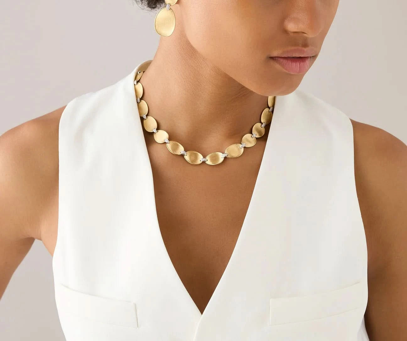 Woman wearing a gold necklace and earrings against a neutral background