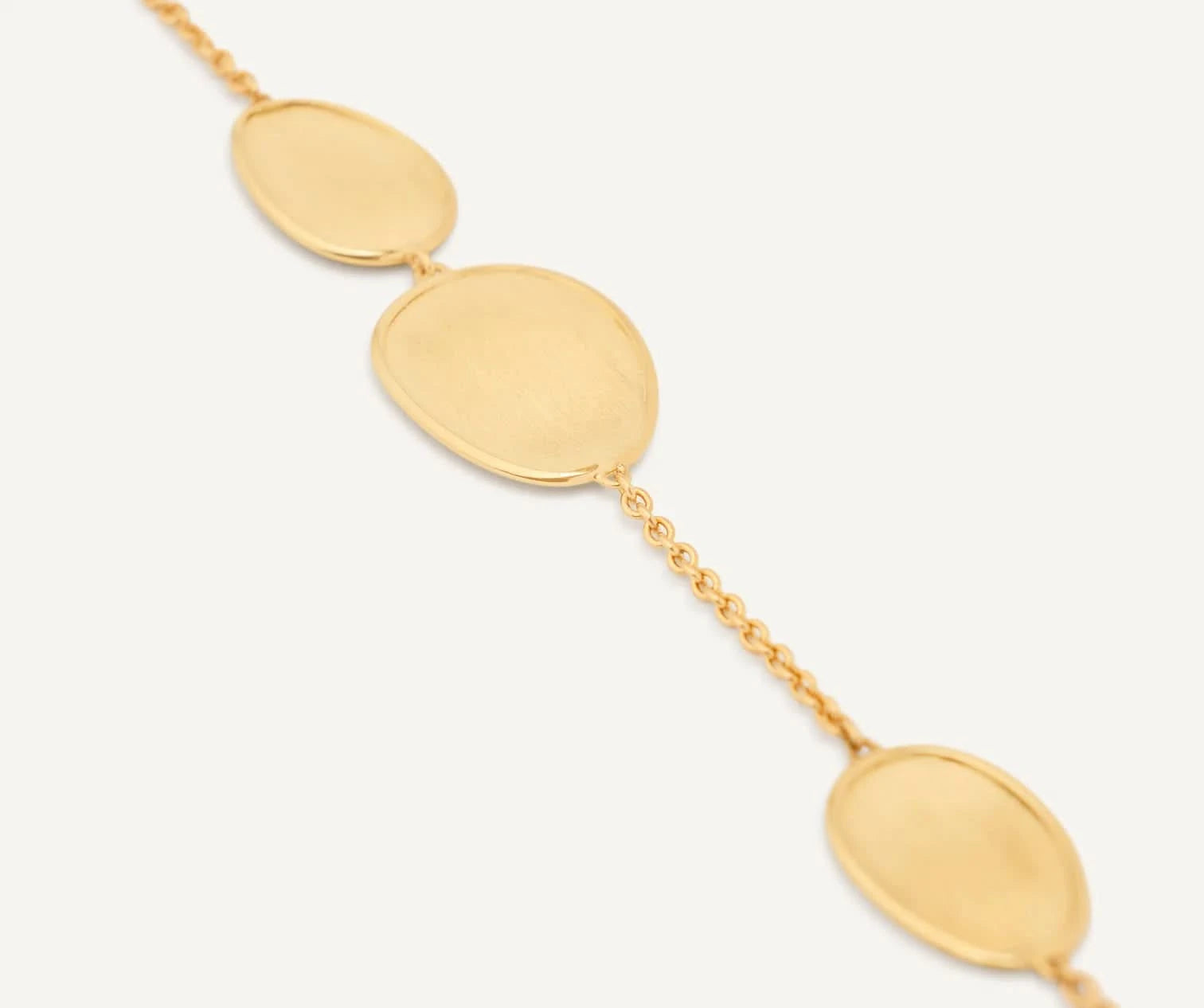 A up close view of the gold chain bracelet featuring three large, flat oval disc charms connected by delicate gold links, shown against a clean off-white background.