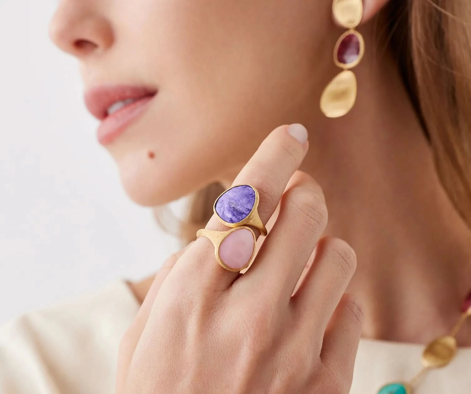 Close-up of a woman's hand wearing a gold ring with purple and pink stones, and gold earrings.