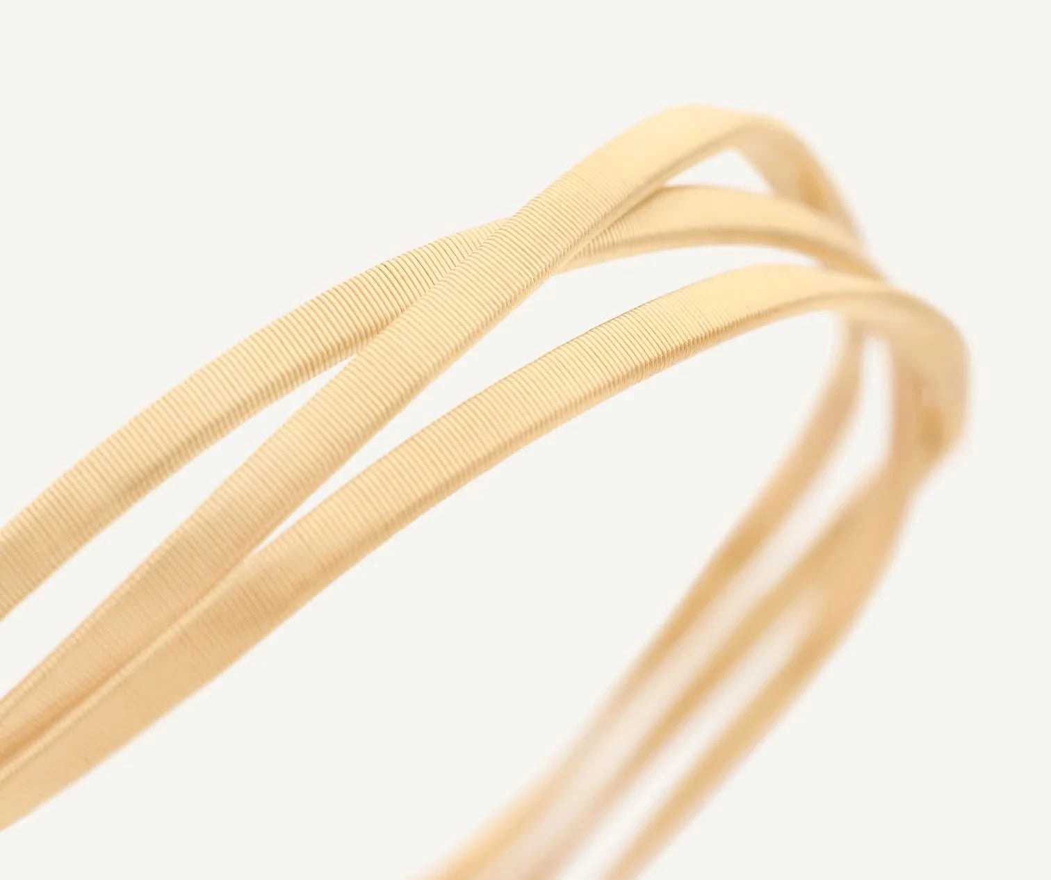 Close-up of gold ribbon bracelet on a light gray background