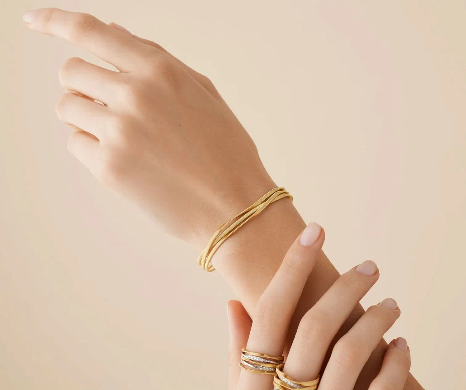 Hand wearing a gold bracelet on a beige background