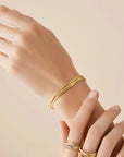 Hand wearing a gold bracelet on a beige background