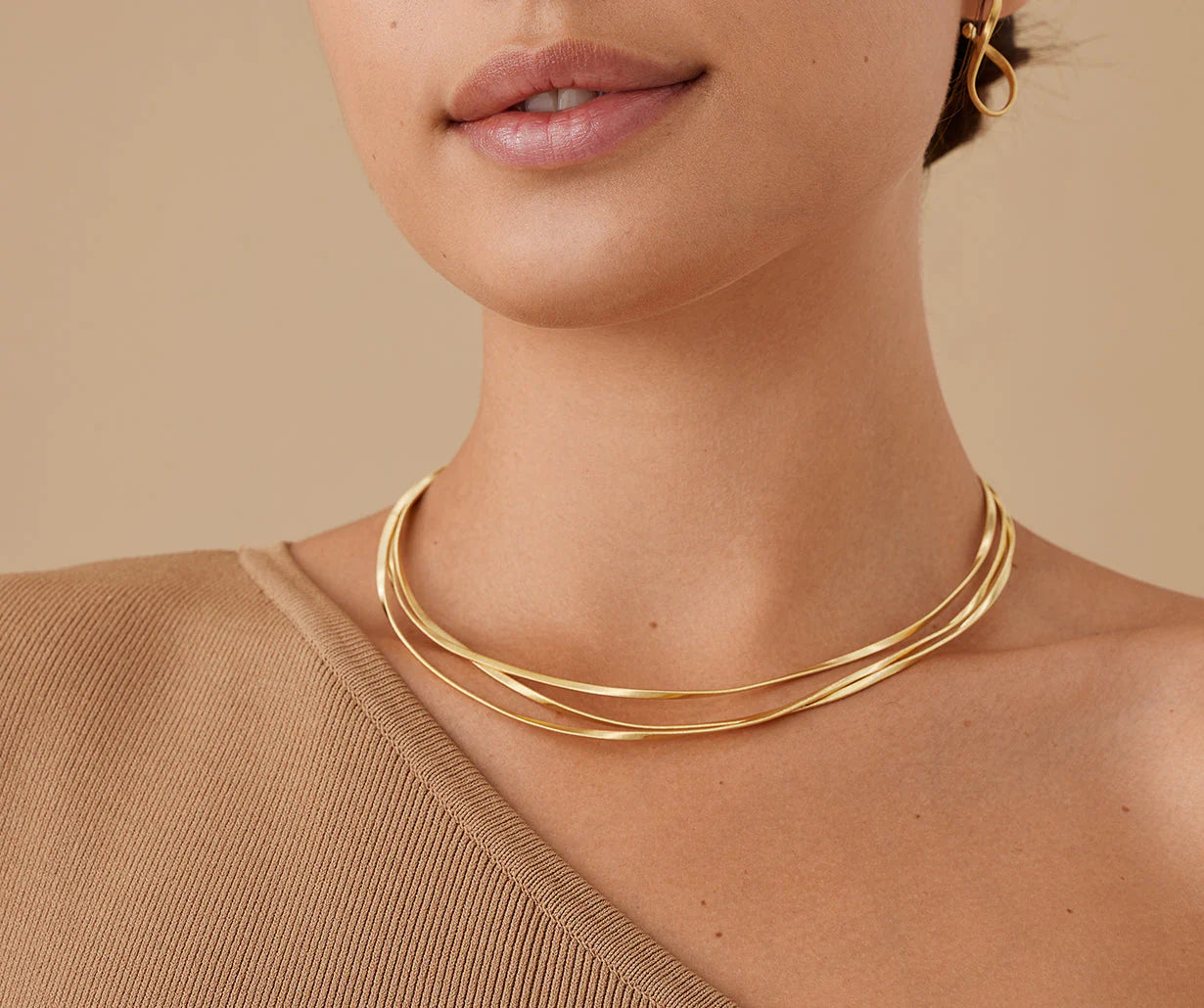 Close-up of a woman wearing a gold necklace and earrings against a beige background