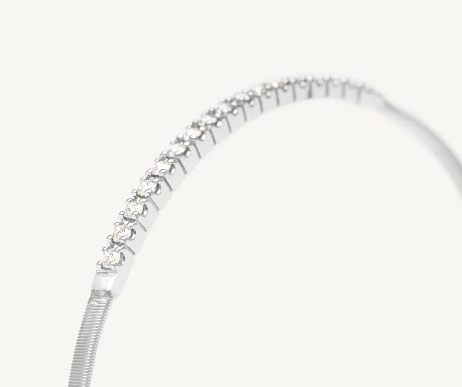 A close-up of a silver-toned snake chain bracelet with a curved row of clear round-cut gemstones along the top, set against a plain off-white background.