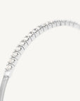 A close-up of a silver-toned snake chain bracelet with a curved row of clear round-cut gemstones along the top, set against a plain off-white background.
