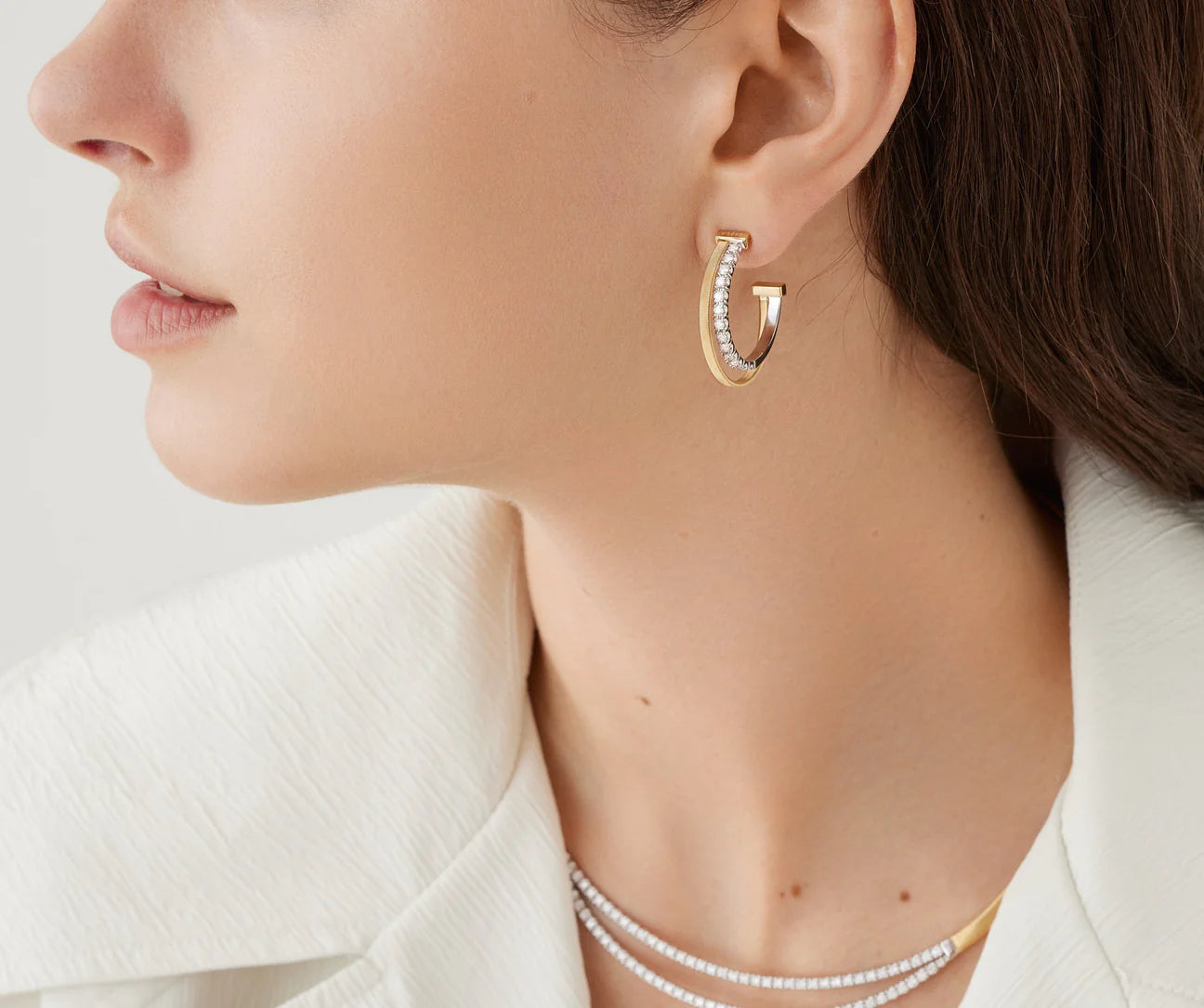 Close-up of a person wearing gold hoop earrings with a white background