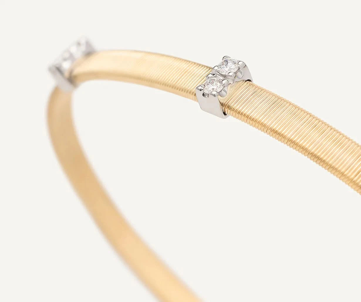A close-up of a gold bangle bracelet with silver-toned end caps, each set with small clear gemstones, on a light off-white background.
