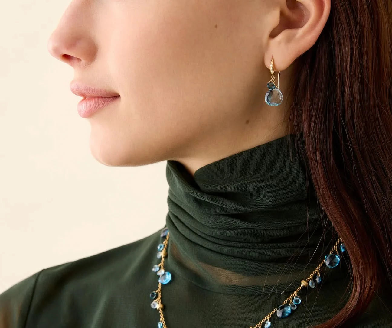 Close-up of a person wearing a green turtleneck and blue beaded necklace with earrings.
