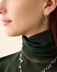 Close-up of a person wearing a green turtleneck and blue beaded necklace with earrings.
