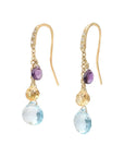 A pair of gold drop earrings featuring a small purple  gemstone, a textured gold gemstone, and a faceted light blue teardrop gemstone, shown against a light off-white background.