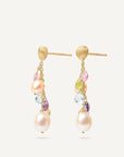 A pair of gold dangle earrings featuring large white freshwater pearls, small multicolored gemstones, and textured gold posts, shown against a light off-white background. angled