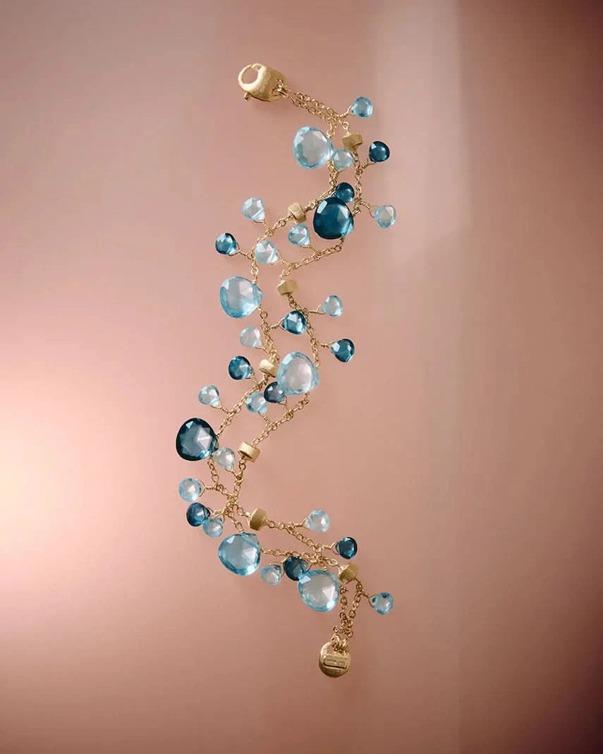 Delicate gold bracelet with blue gemstones on a gradient pink background