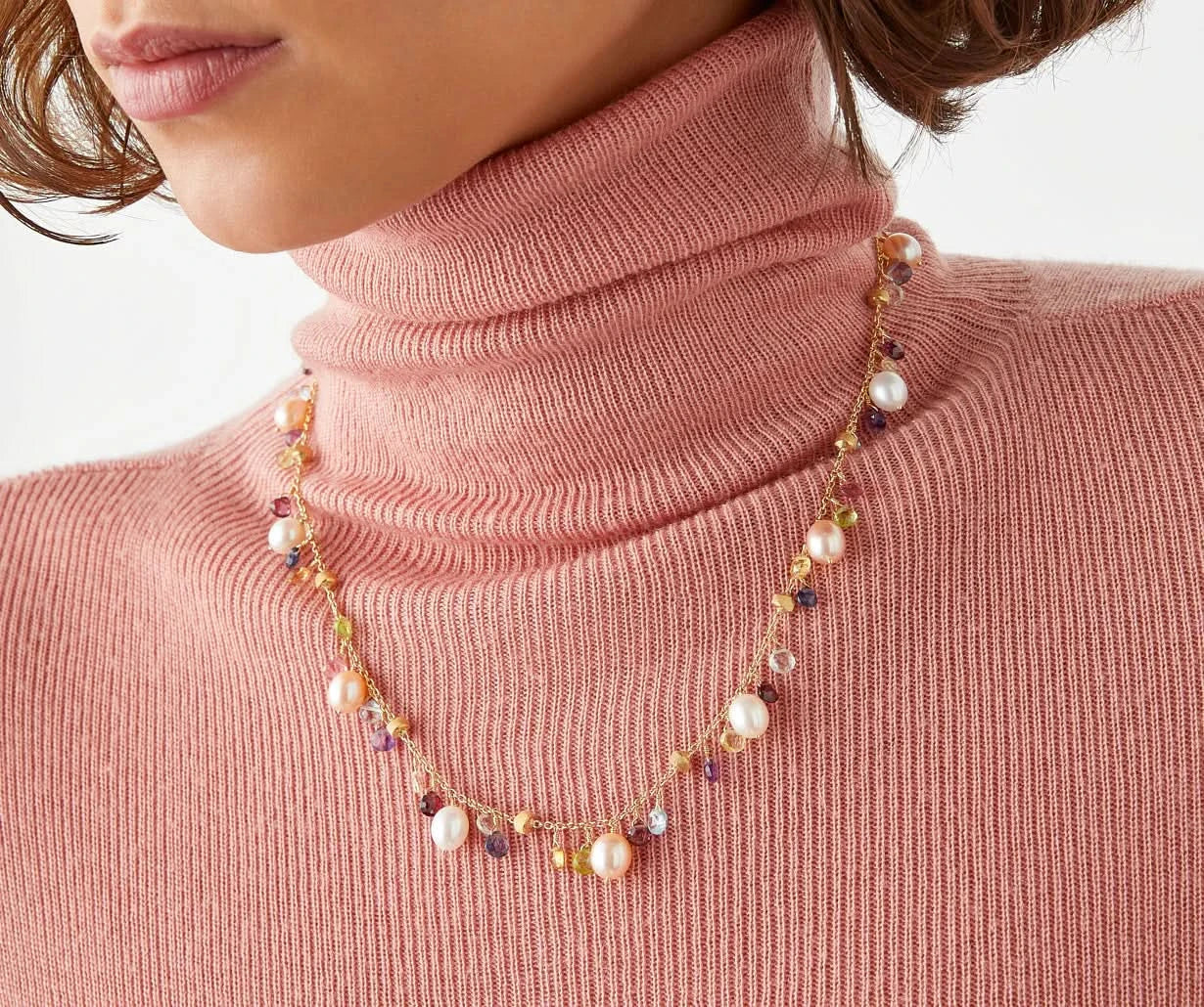 Necklace with multicolored beads worn by a person in a pink turtleneck.