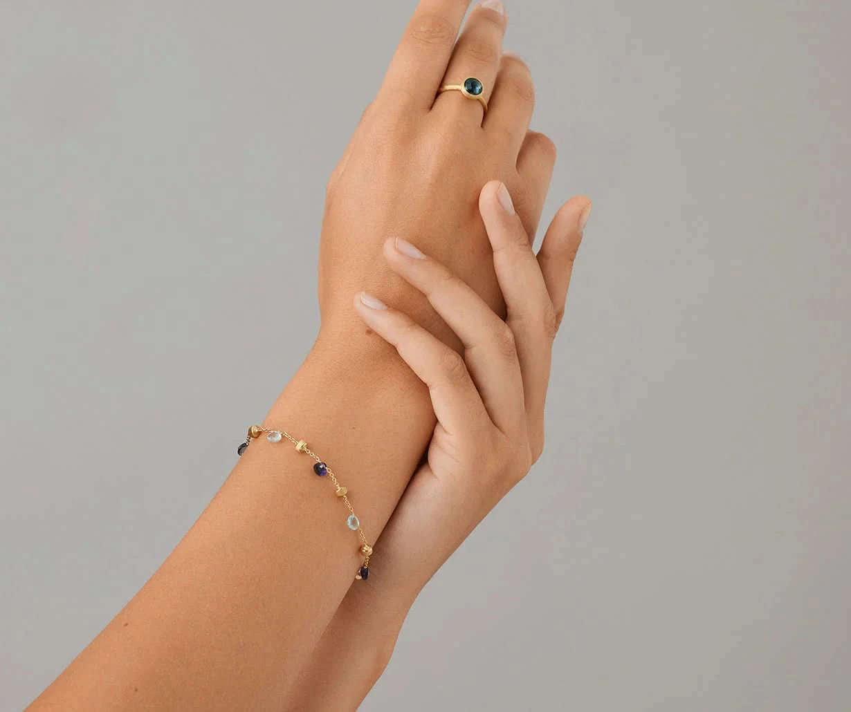 Hand wearing a gold bracelet with small beads on a gray background