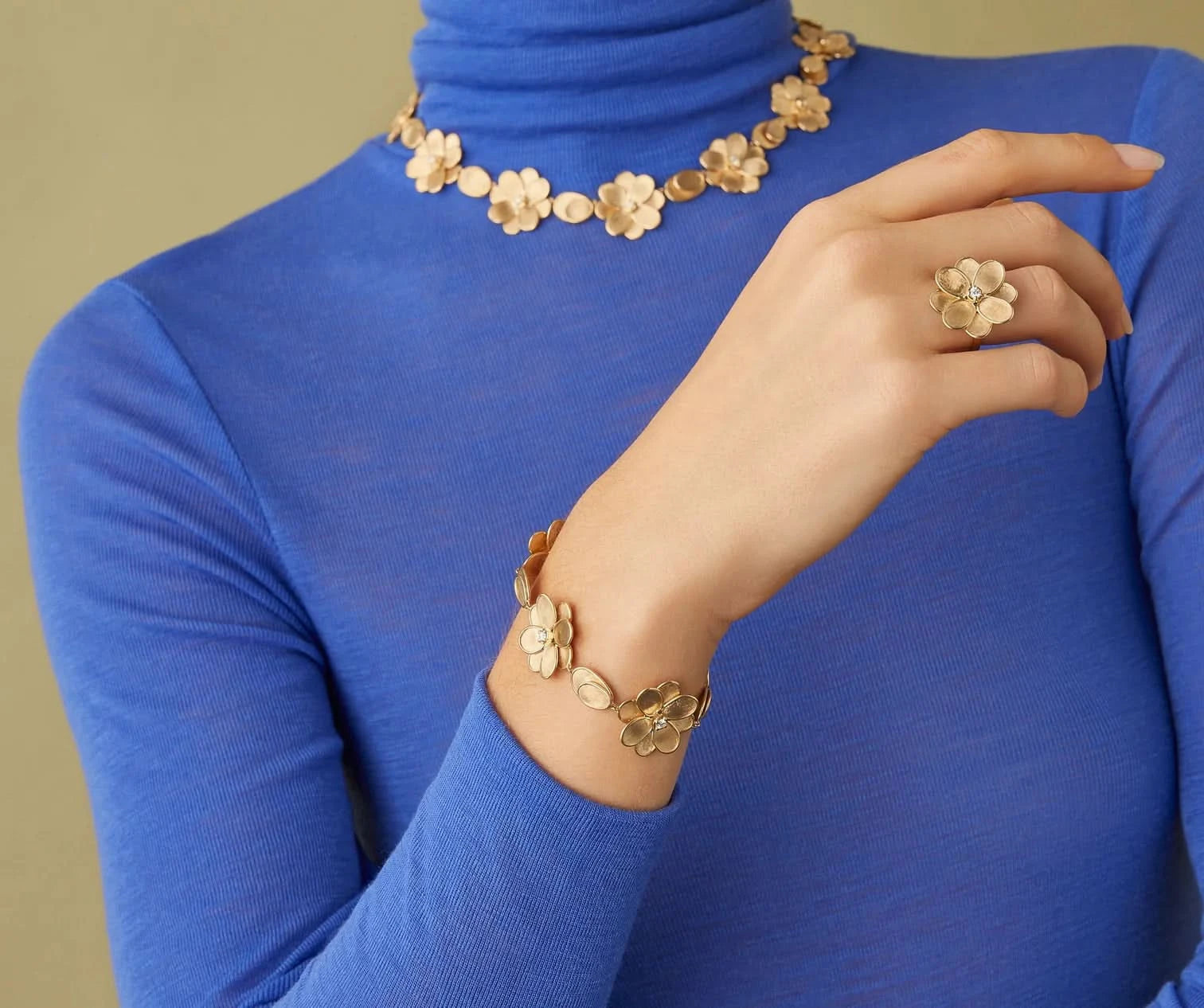 Gold floral jewelry set including necklace, bracelet, and ring on a blue turtleneck background