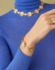 Gold floral jewelry set including necklace, bracelet, and ring on a blue turtleneck background