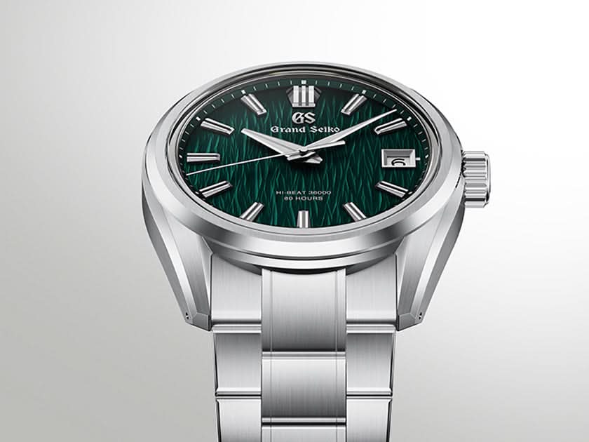 A Grand Seiko stainless steel watch with a textured dark green dial, silver-tone case, and matching metal link bracelet, shown on a light gray gradient background.