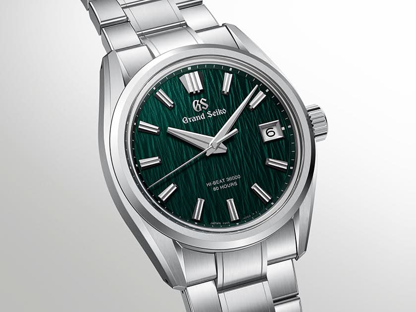 A Grand Seiko wristwatch with a polished silver-tone stainless steel case and bracelet, featuring a textured dark green dial with silver-tone indices and a date window.