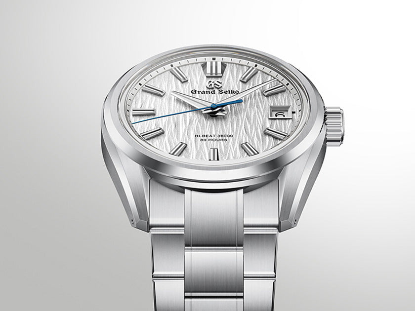 A Grand Seiko stainless steel watch with a textured silver dial, silver-tone case, and matching link bracelet, shown against a light gray gradient background.