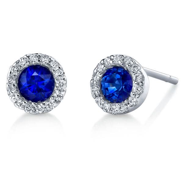 A pair of Stanton Color gemstone stud earrings crafted in 14kt white gold, each featuring a rich blue sapphire center stone encircled by a radiant white diamond halo borders on a white background.