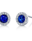 A pair of Stanton Color gemstone stud earrings crafted in 14kt white gold, each featuring a rich blue sapphire center stone encircled by a radiant white diamond halo borders on a white background.