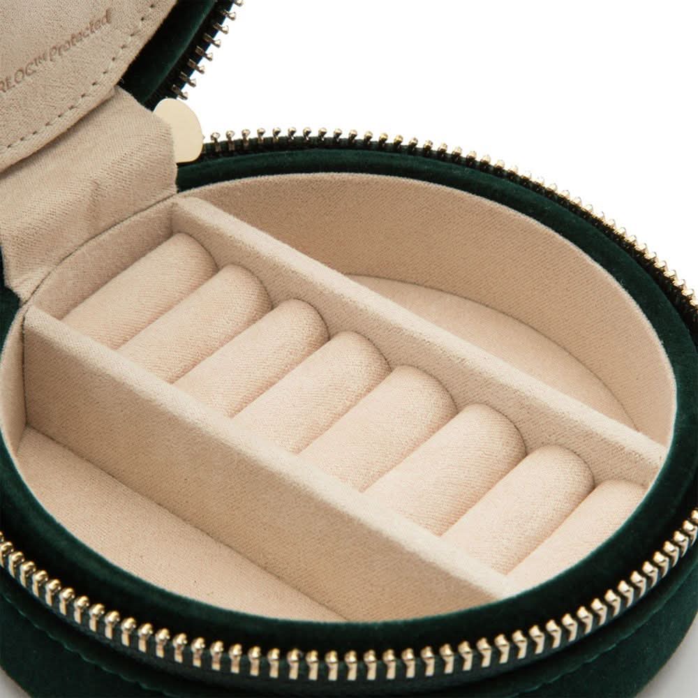 Round jewelry case with beige interior and gold zipper on a white background