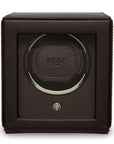 A dark brown leather-wrapped watch winder box with a clear front window showing a single watch winding carousel inside. The center features a circular leather patch with the embossed brand name 'WOLF'.