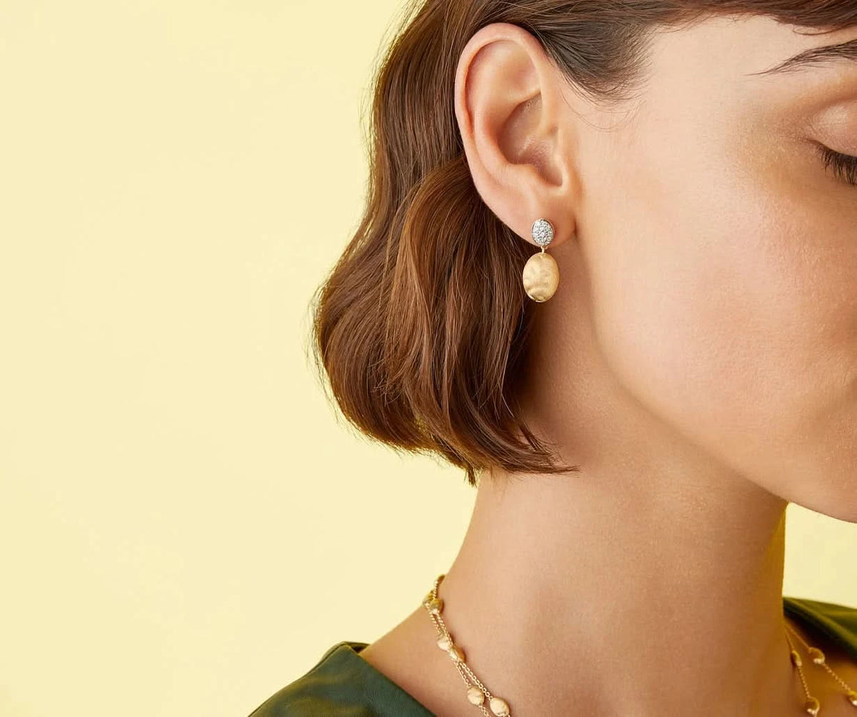 Close-up of a woman wearing gold earrings and a necklace against a yellow background