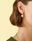 Close-up of a woman wearing gold earrings and a necklace against a yellow background