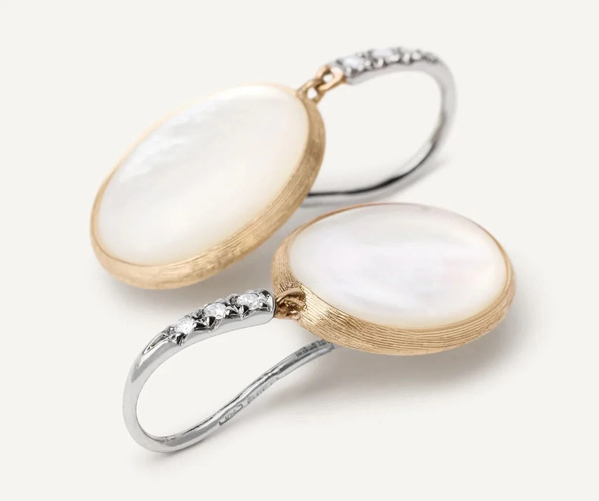 Two earrings with white mother of pearl stones and gold on a light background