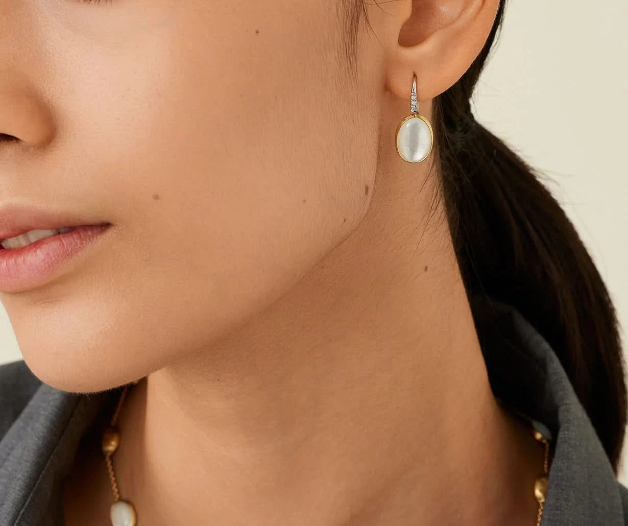 Close-up of a woman wearing pearl earrings with a neutral background