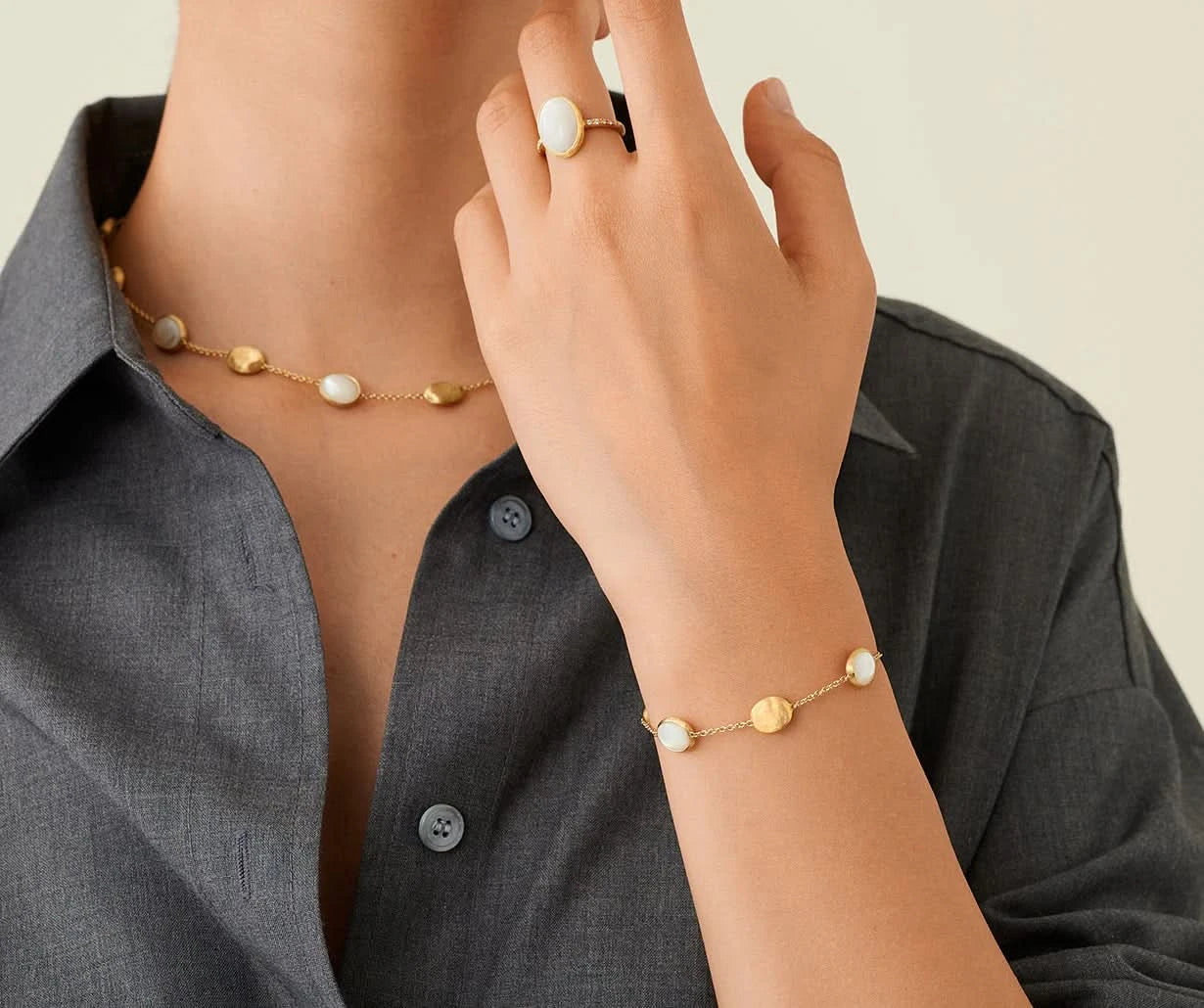 Person wearing a gold necklace and bracelet with small stones, against a neutral background.
