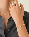 Person wearing a gold necklace and bracelet with small stones, against a neutral background.