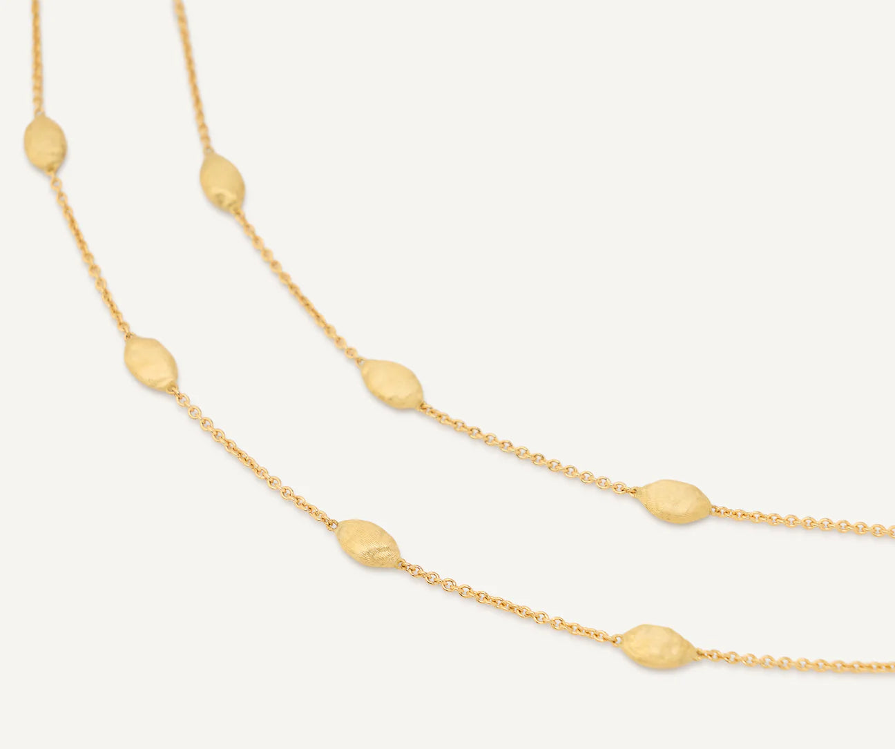 Gold necklace with small beads on a light gray background close up