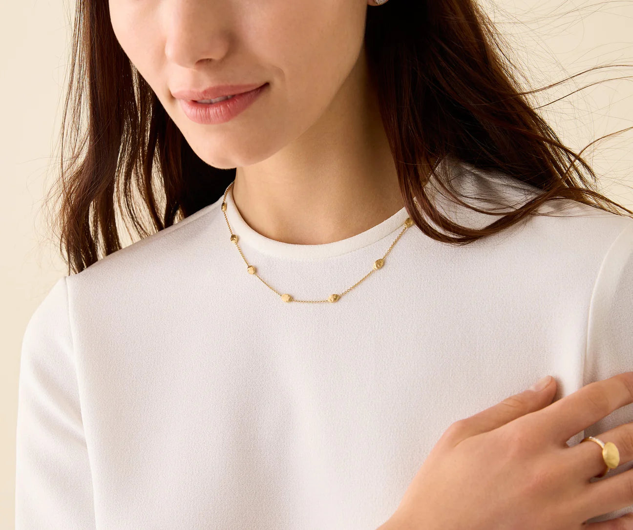 Woman wearing a gold necklace and ring on a plain background
