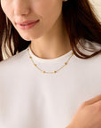 Woman wearing a gold necklace and ring on a plain background