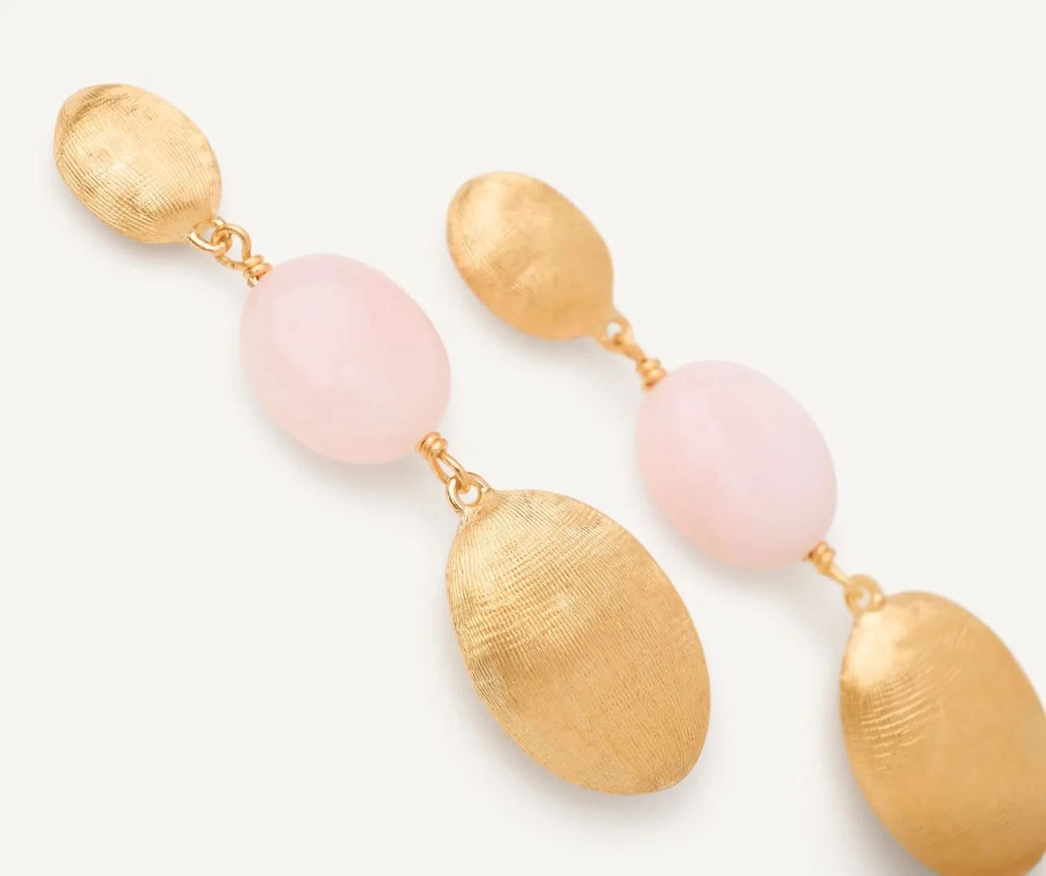 A pair of gold and pink drop earrings with textured oval gold tops and smooth light pink oval beads, shown on a clean off-white background.